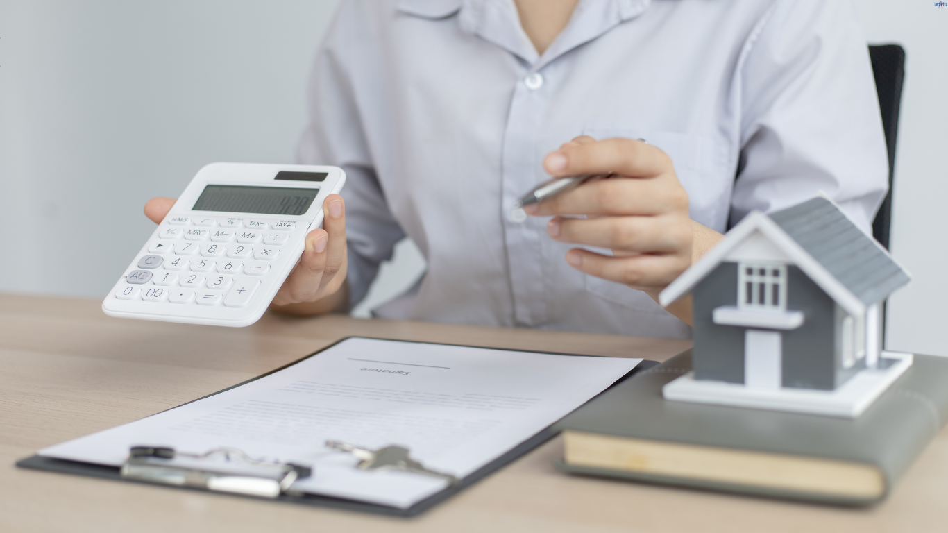 Man Holding Calculator and a Paper and House Miniature on the Table